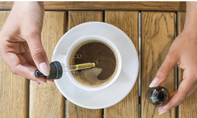 A hand squeezing CBD oil into a cup of coffee