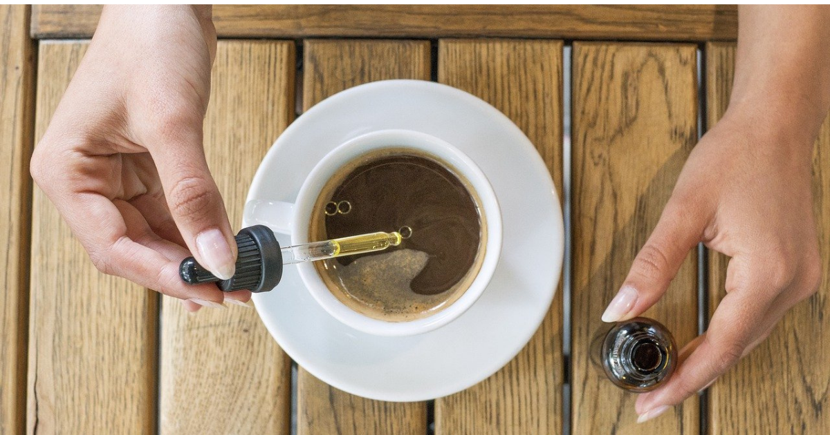 A hand squeezing CBD oil into a cup of coffee