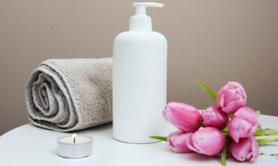 A light brown towel rolled up next to a white lotion bottle. There is a small night light and pink rose on other side of the lotion