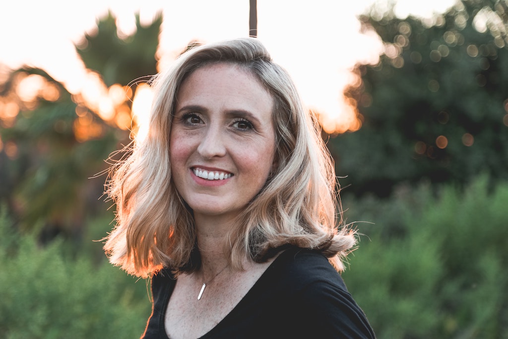 Middle aged woman with shoulder length blonde hair smiles as the sun sets behind her