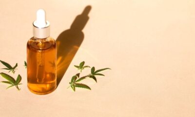 A brown glass bottle with a white lid stands on a pale background, with green leaves on two sides.