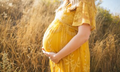 A woman in a yellow dress holding a pregnancy bump while standing in a field