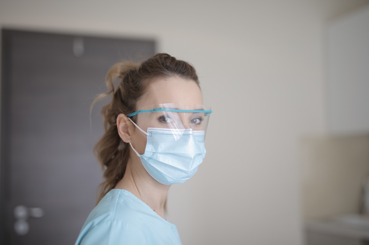 Woman wearing blue face mask and hospital scrubs looks at the camera