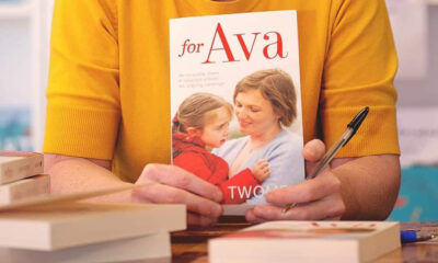 A person wearing a yellow sweater holds the cover of a book to the camera