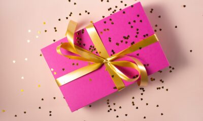 A present wrapped in pink paper with a gold ribbon and bow. There is glitter sprinkled across the top