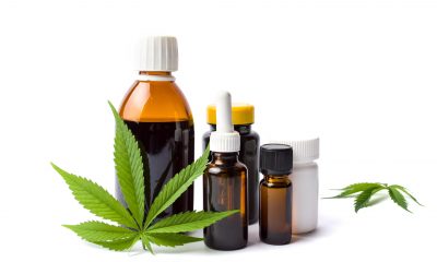 A green cannabis leaf is stood against a brown medicine bottle