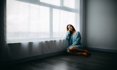 A woman sits on the floor near a large window covered with a voile curtain