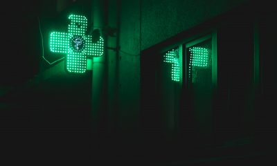green pharmacy symbol in the shape of a cross is alight on a dark night