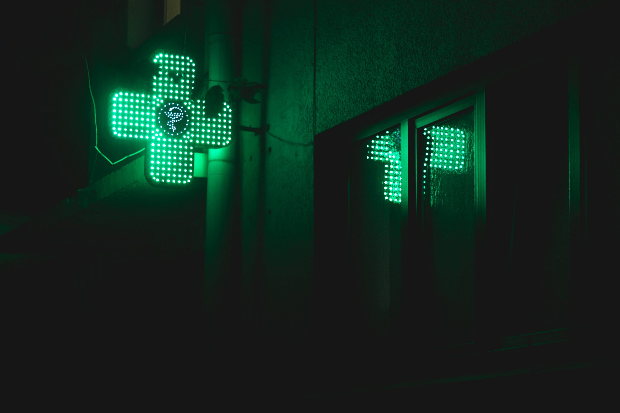green pharmacy symbol in the shape of a cross is alight on a dark night