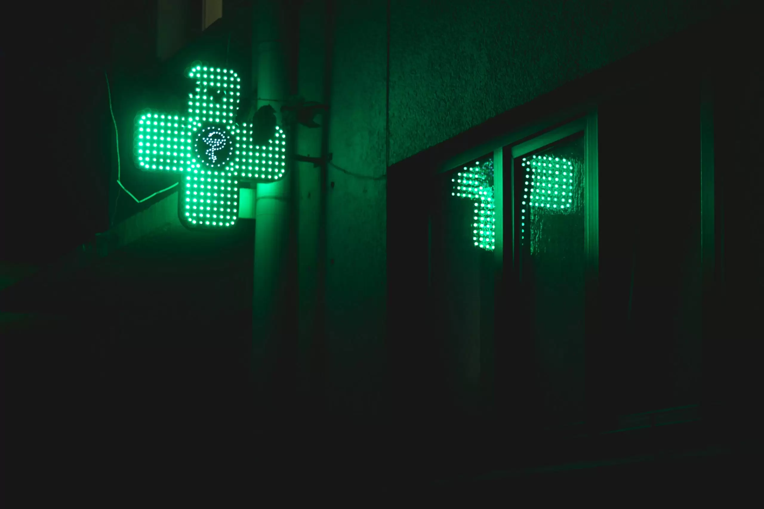 green pharmacy symbol in the shape of a cross is alight on a dark night