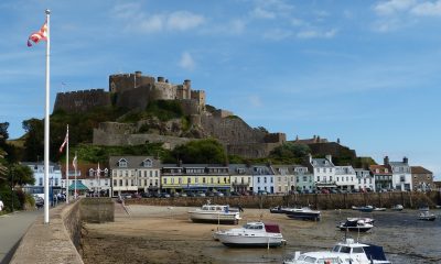 A stone castle sits atop a hill overlooking a harbour in Jersey
