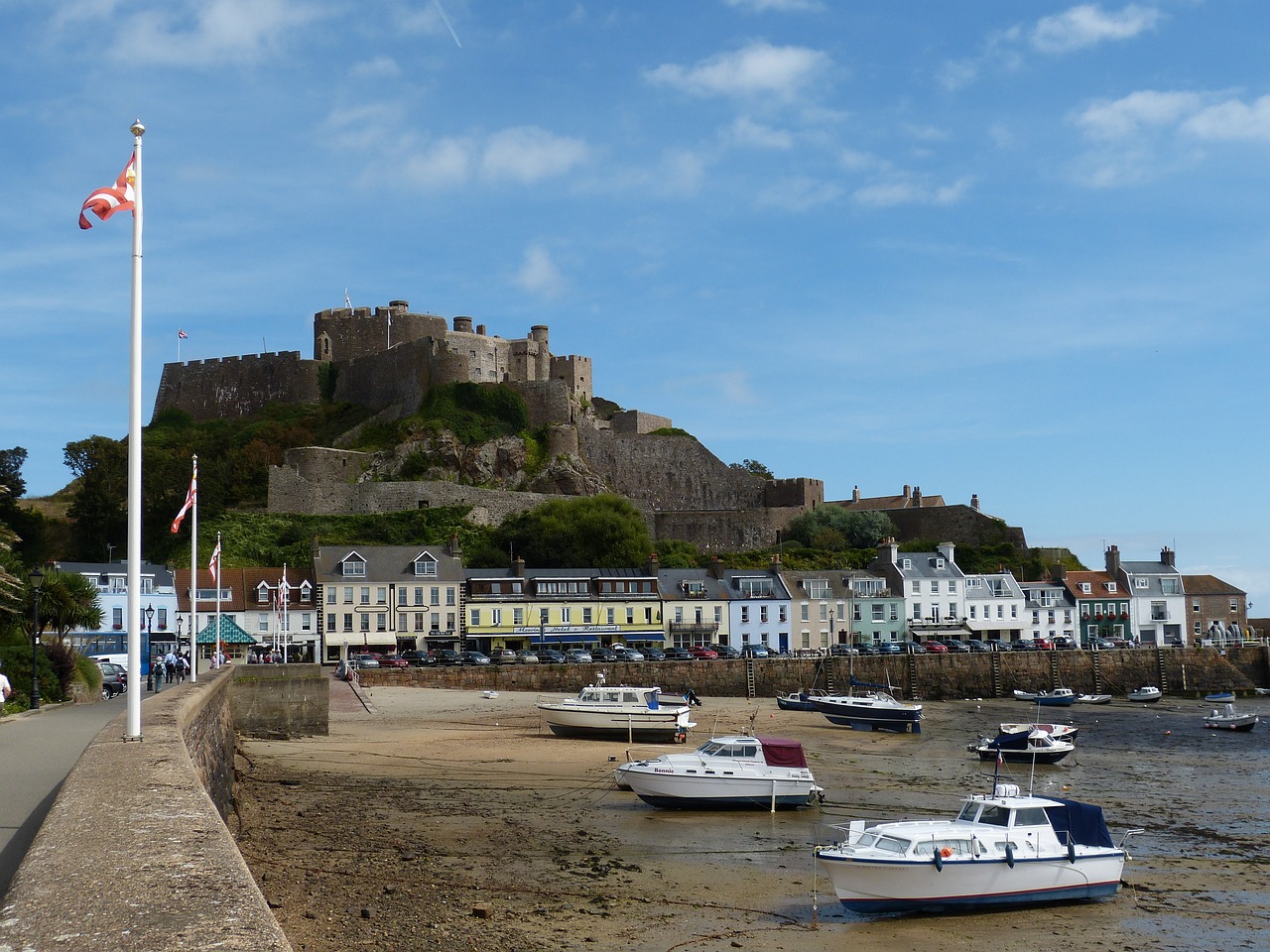 A stone castle sits atop a hill overlooking a harbour in Jersey