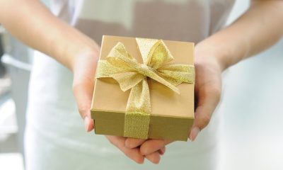 A woman's hands holding a gold gift box for Mother's Day with a gold ribbon on it.