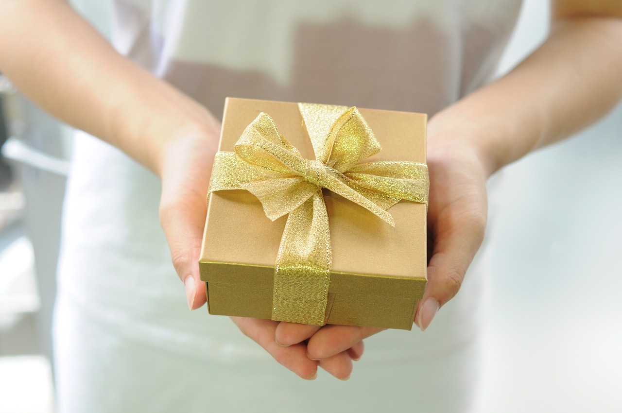 A woman's hands holding a gold gift box for Mother's Day with a gold ribbon on it.