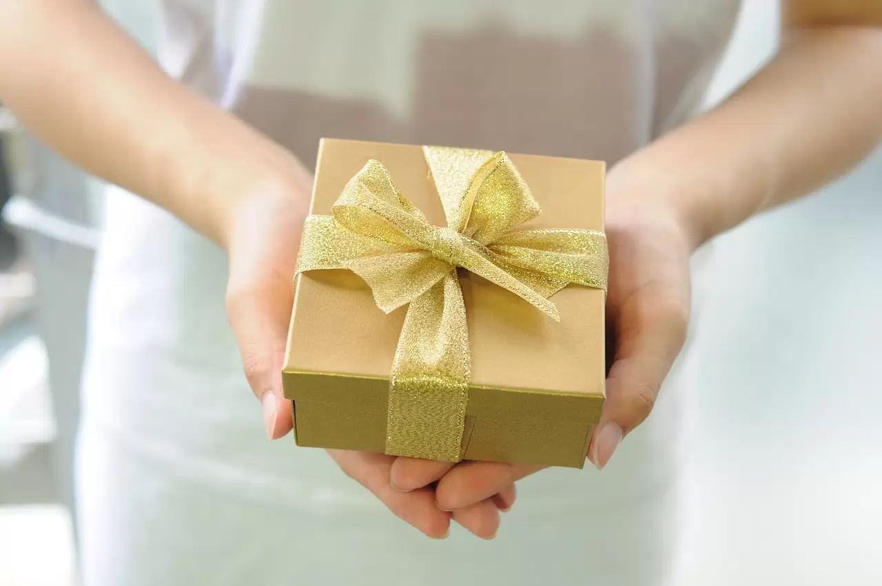 A woman's hands holding a gold gift box for Mother's Day with a gold ribbon on it.