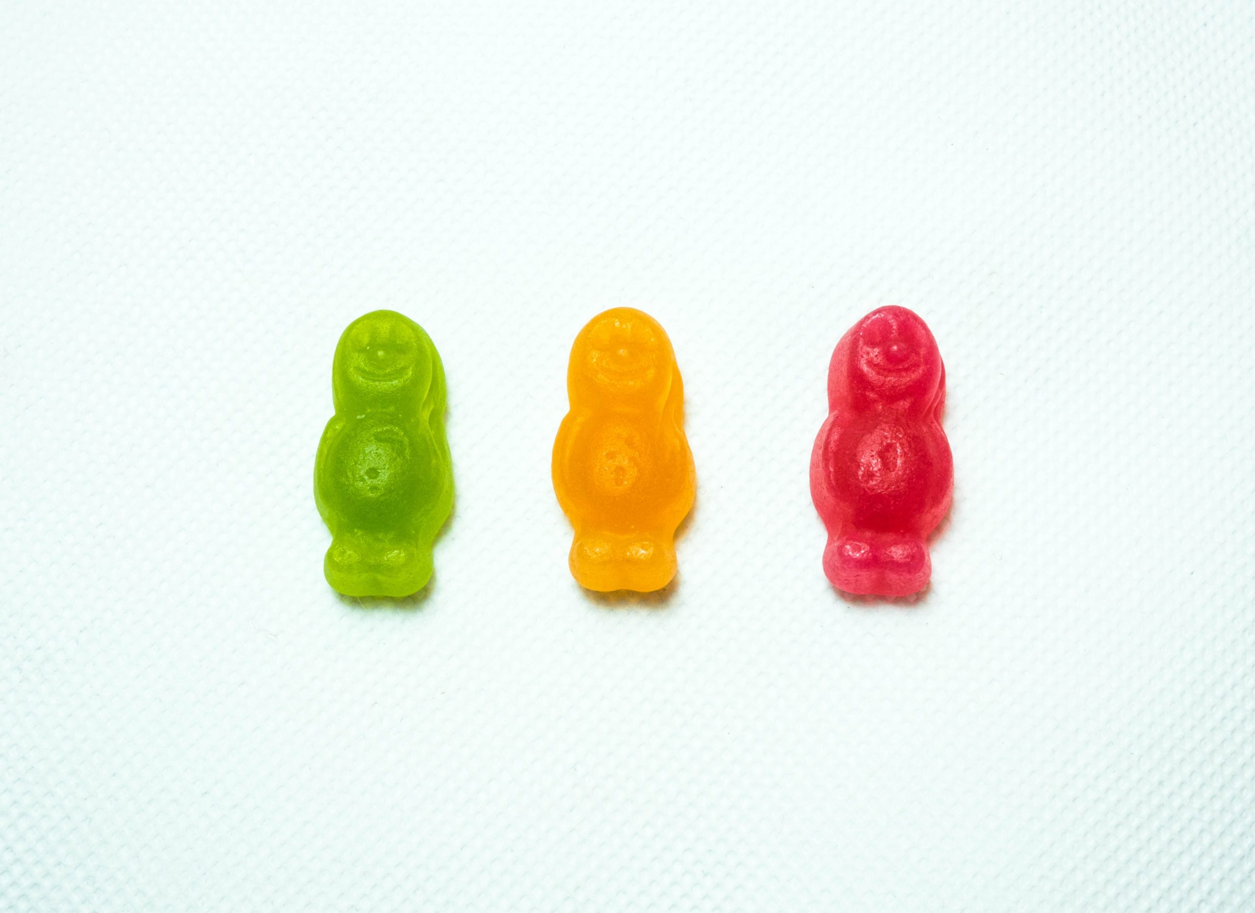 Three gummy men candies in a row on a white background