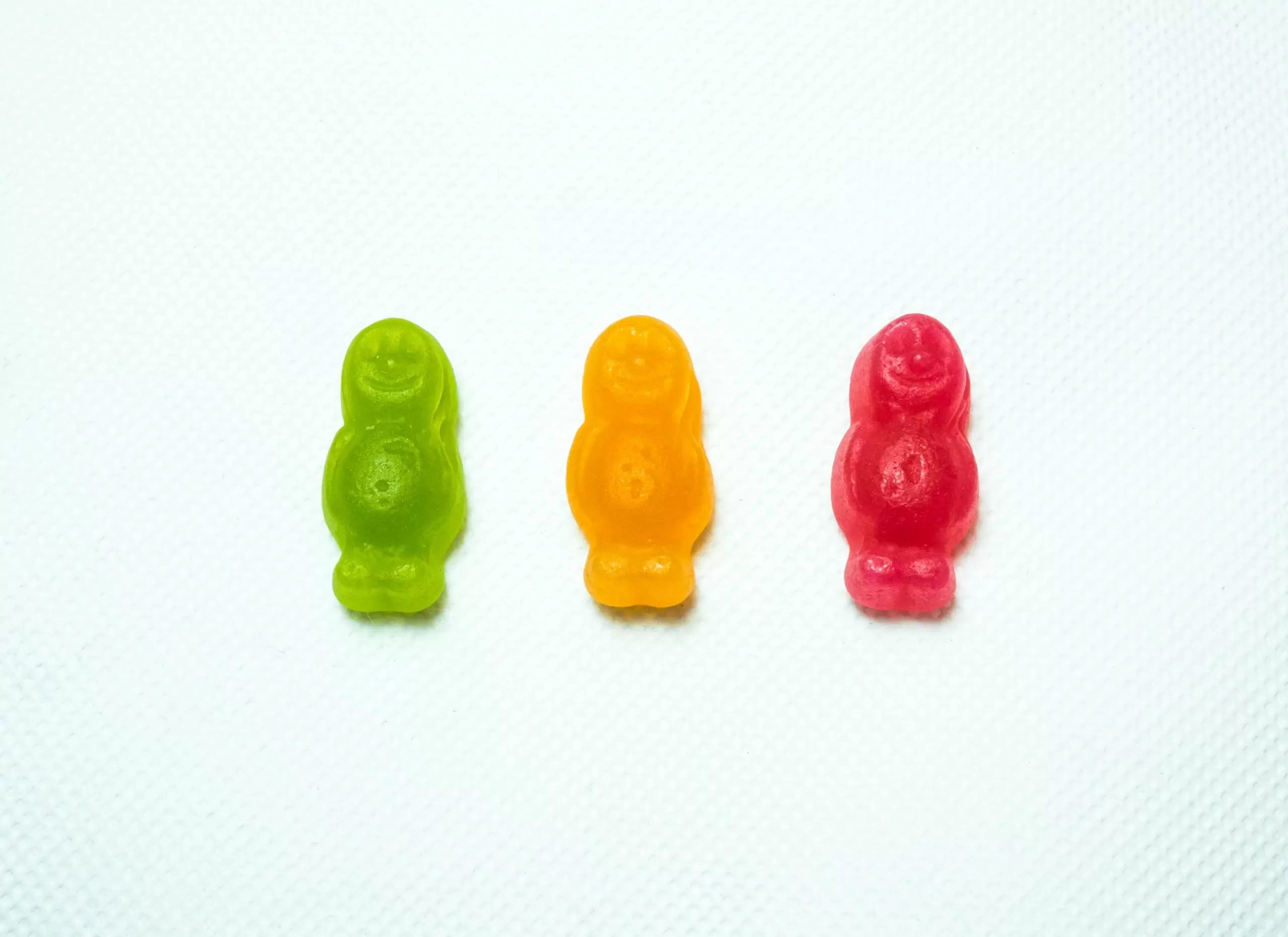 Three gummy men candies in a row on a white background