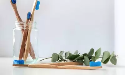 Four wooden toothbrushes in a glass jar with a sprig of ivy near them