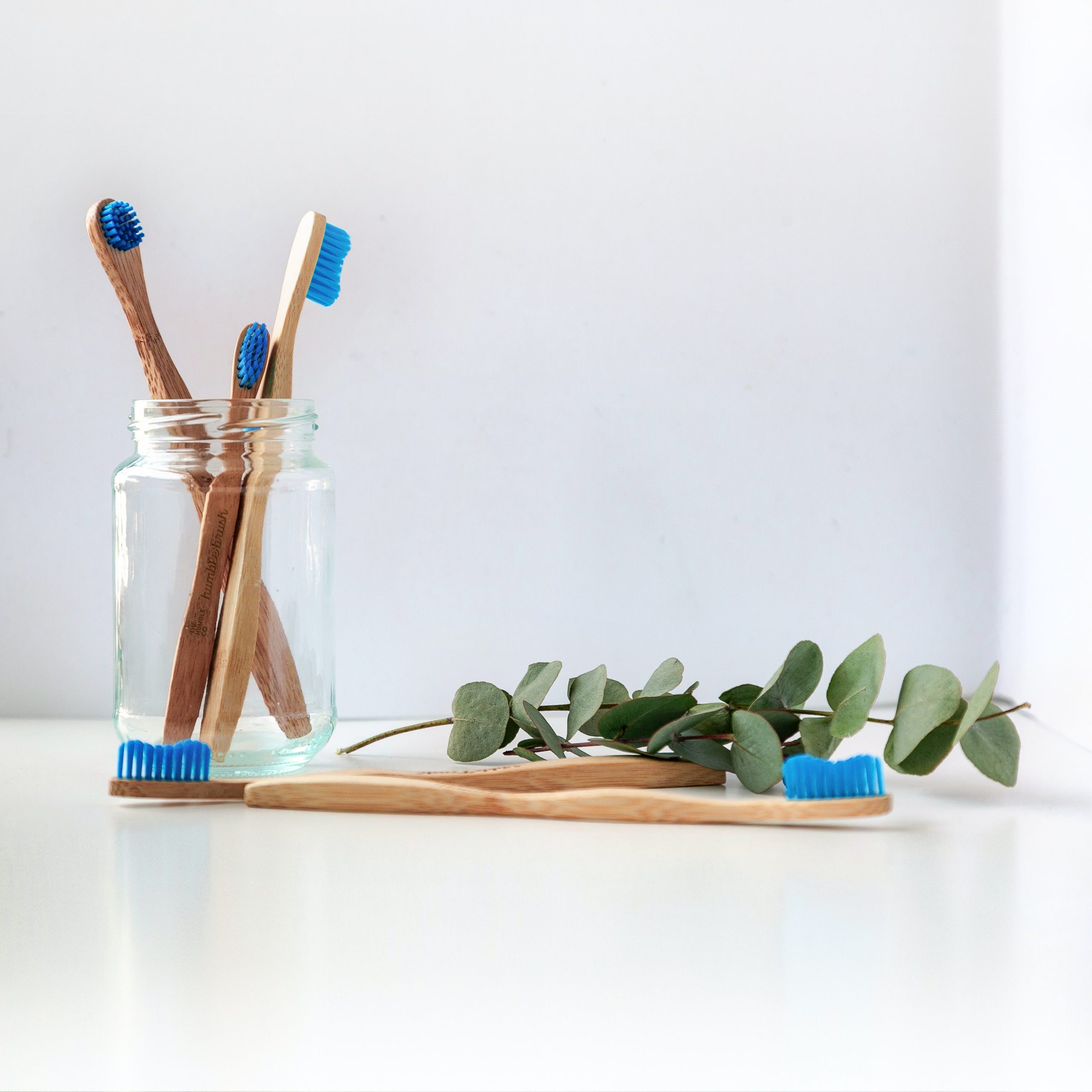 Four wooden toothbrushes in a glass jar with a sprig of ivy near them