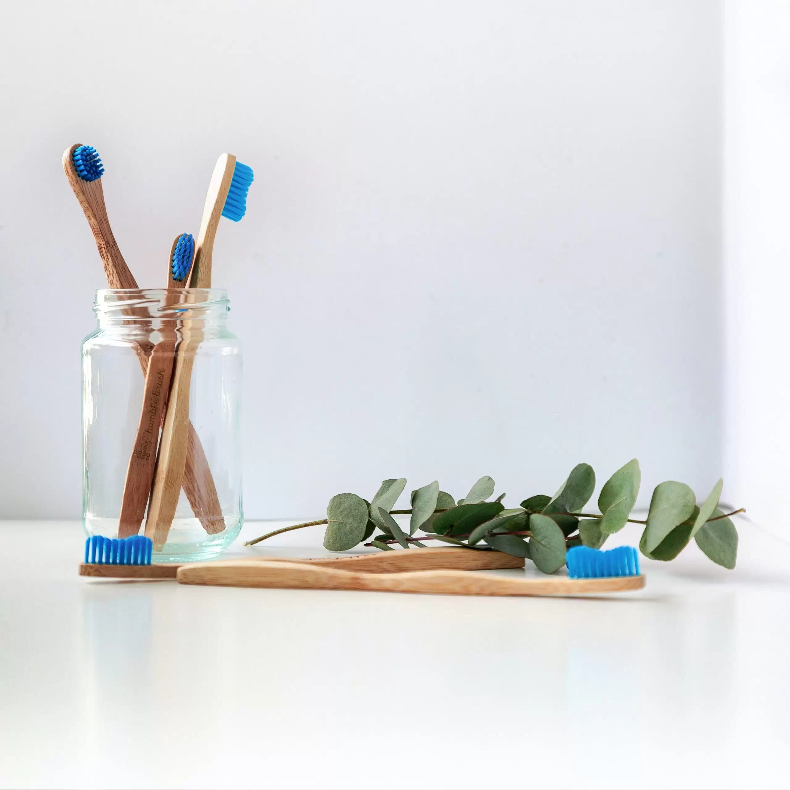 Four wooden toothbrushes in a glass jar with a sprig of ivy near them
