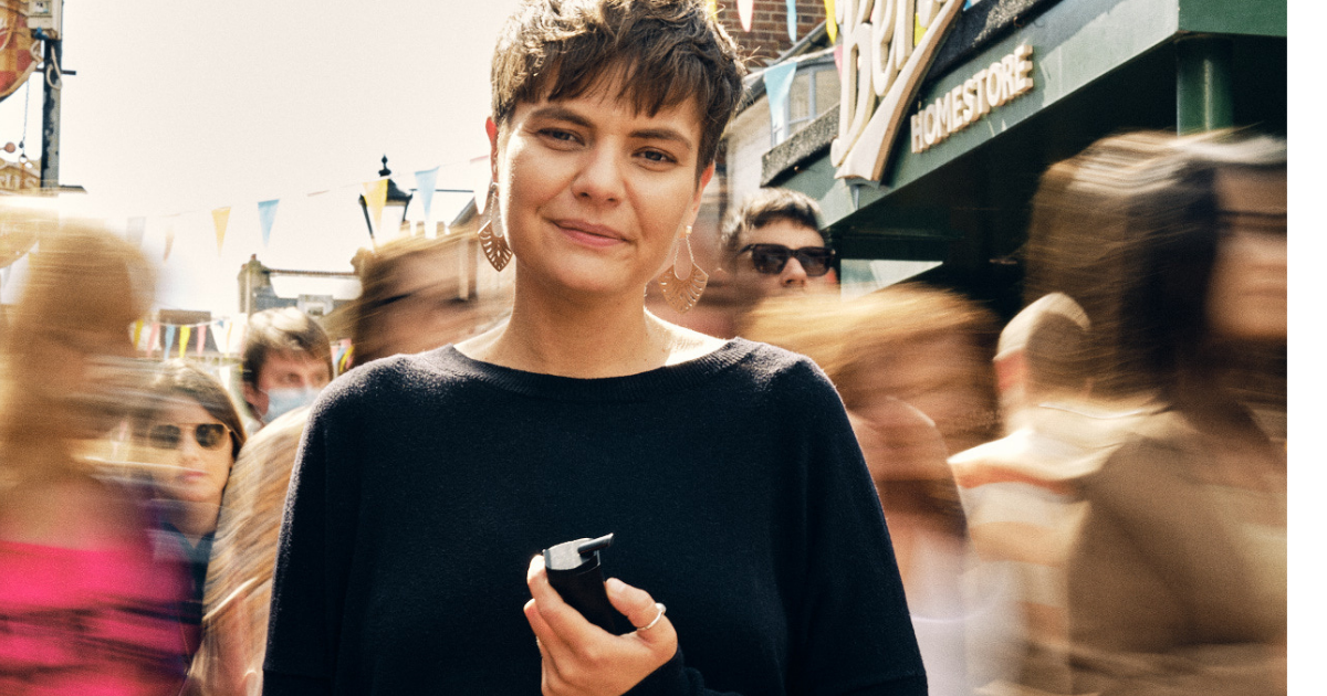 A woman holding a black vape device on a busy street