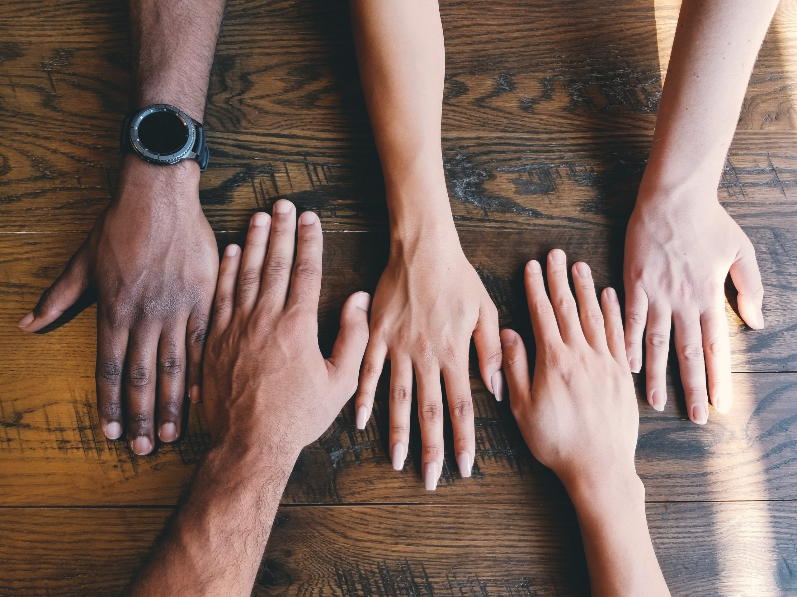 Two rows of hands on a wooden table in lines