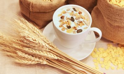 Gold grains lying next to a cup of tea which has nuts on the top of the milk.