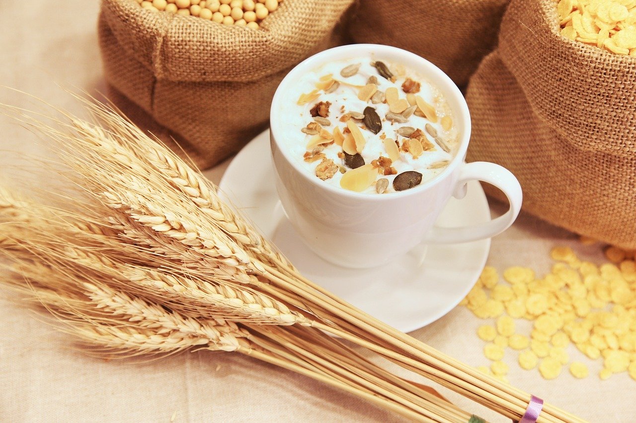 Gold grains lying next to a cup of tea which has nuts on the top of the milk.