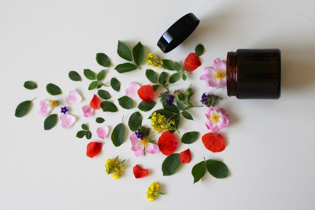 A brown jar lying on its side. The contents are spilling out on the left hand side of the photo. It contains a lot of leaves and flowers on a white background.