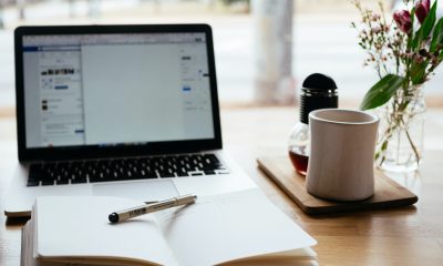 A notepad sits in front of a computer where a brand are applying for funding for their company. They also have a white teacup next to flowers