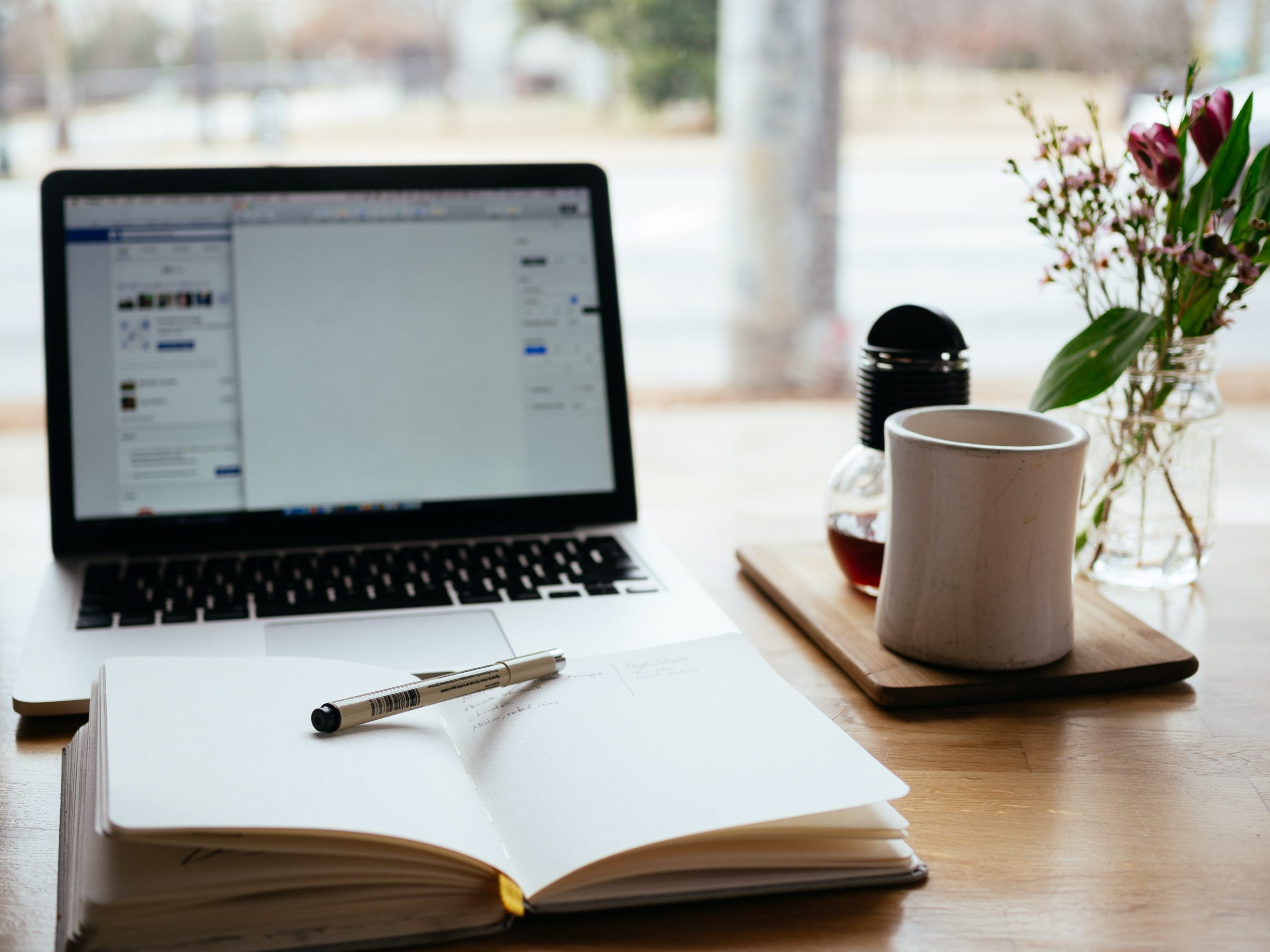 A notepad sits in front of a computer where a brand are applying for funding for their company. They also have a white teacup next to flowers