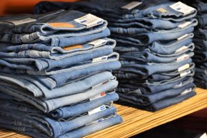 Two piles of blue denim jeans on a wooden shelf lined up to be sold.