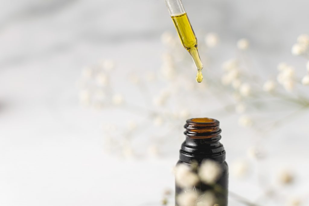 A bottle of CBD oil against white background with white flowers to highlight its effectiveness against Alzheimer's Disease