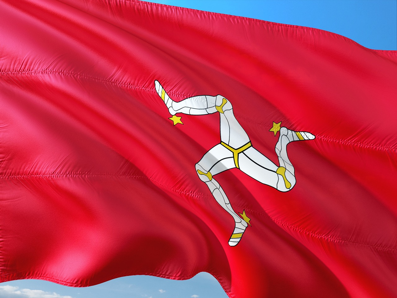 A red Isle of Man flag with three white legs against a blue sky