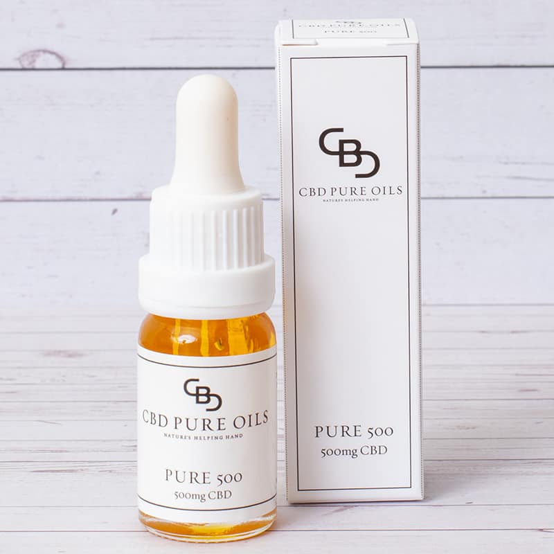 A bottle of CBD Pure Oils Pure 500 CBD Oil next to the products box. They are placed on a wooden table, with a wooden background. 